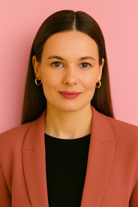 Tummatukkainen ja vaaleaihoinen pienesti hymyilevä nainen, jolla päällä jakkupuku.