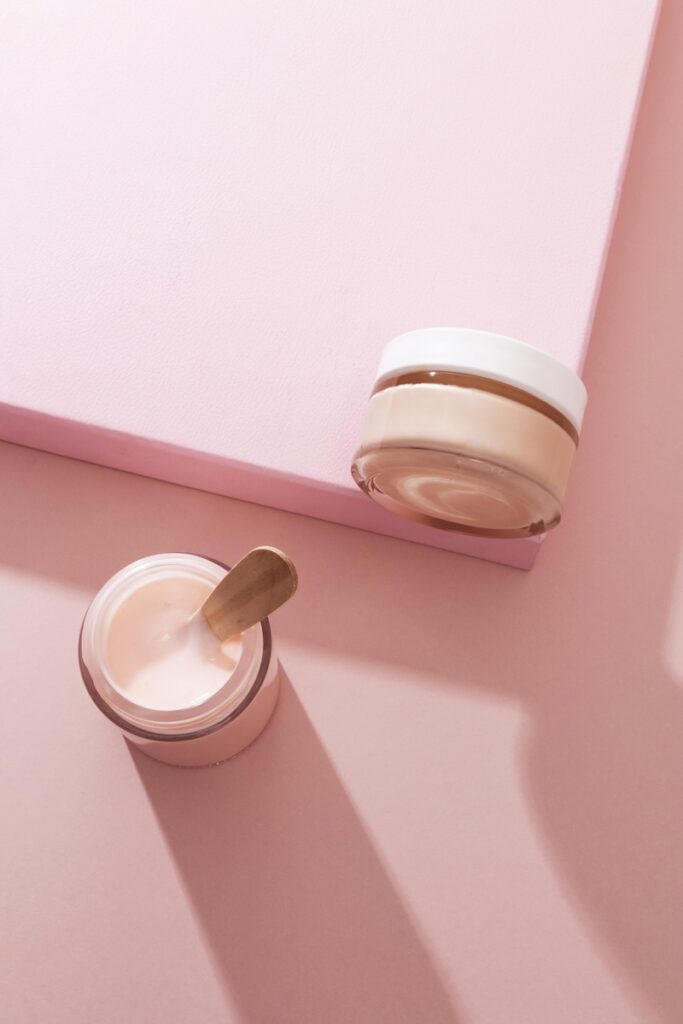 Kaksi vaaleanpunaista kosmetiikkapurkkia vaaleanpunaisella pinnalla.